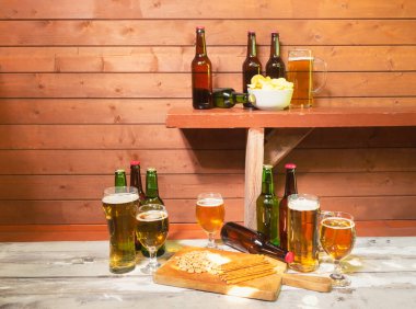 Bira şişeleri, patates cipsi ve bira kupası, bir bardak bira, bir kupa bira, fıstık, tuzlanmış saman ve bira şişeleri güneşli bir günde eski tahta tahtada. Kopyalama alanı ile göster.