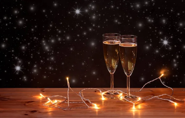シャンパンと暗い背景に輝くクリスマスライト付きのメガネ 選択的フォーカス コピースペースで見る — ストック写真