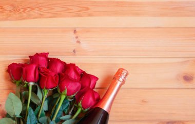 Bir şişe şampanya ve ahşap arka planda kırmızı güller. Kopyalama alanı olan üst görünüm.