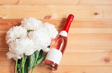 Bir şişe gül şampanyası ve tahta arka planda beyaz şakayıklar. Üst görünüm, alanı kopyala.