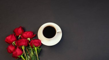 Bir fincan kahve ve koyu arkaplanda kırmızı güller. Üst görünüm, alanı kopyala.