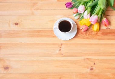 Beyaz bir fincan kahve ve ahşap masada renkli taze bahar laleleri. Üst görünüm, alanı kopyala.