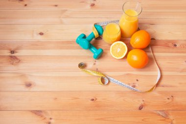 Sürahi ve bir bardak portakal suyu, dambıl, mezura ve taze portakallar masanın yanında. Kopyalama alanı olan üst görünüm.