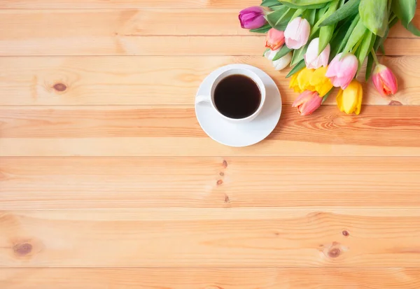 Beyaz bir fincan kahve ve ahşap masada renkli taze bahar laleleri. Üst görünüm, alanı kopyala.