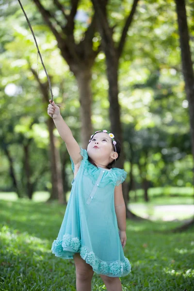 Liten asiatisk tjej spelar gren av träd i trädgården — Stockfoto