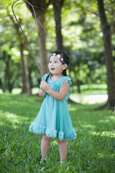 Liten asiatisk tjej spelar gren av träd i trädgården — Stockfoto