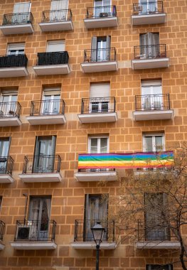 Balkonunda eşcinsel bayrağı olan bir binanın ön cephesi.