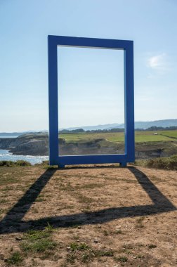 A blue square frame on the edge of a cliff with a landscape behind