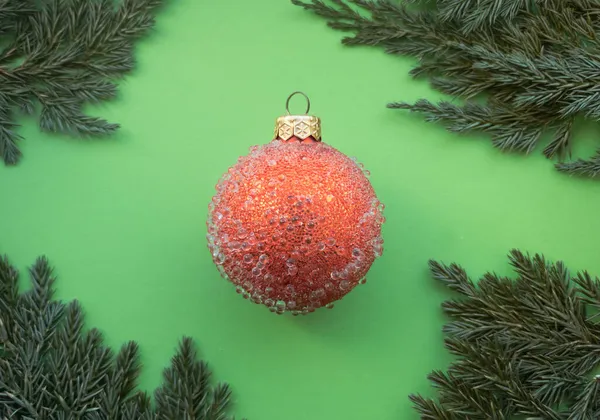 Palla di Natale rossa con alcuni dossi e ramoscello di abete rosso su uno sfondo verde. Design natalizio minimale — Foto Stock