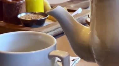 Lokantadaki bir masaya yakın plan beyaz çaydanlıktan beyaz fincana yeşil çay döktü.