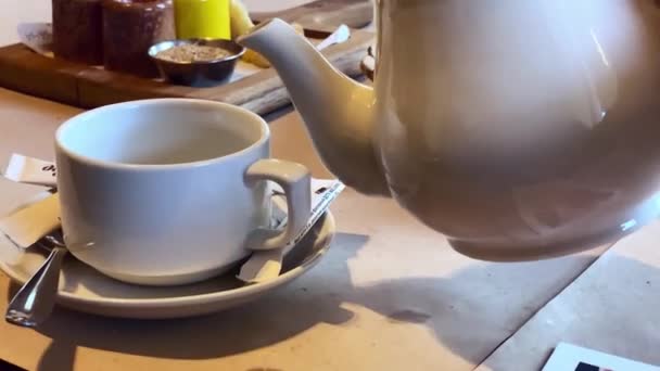 식당의 탁자 위에 가까이 다가가서 흰 찻주전자에서 녹차를 하얀 컵에 부었습니다. — 비디오