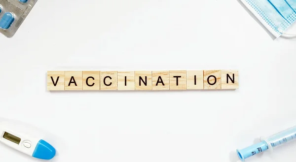 Elrendezés a szó vakcinázás készült fa betűkkel, és közel egy fecskendő, hőmérő, gyógyszer maszk és tabletták — Stock Fotó