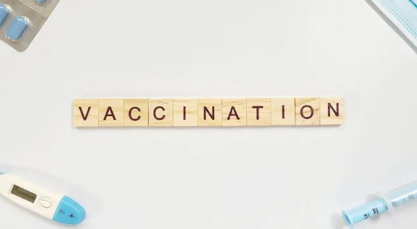 Mise en page avec le mot vaccination fait à partir de lettres en bois et près d'une seringue, thermomètre, masque de médicament et pilules — Photo