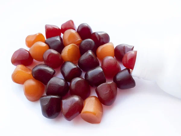 Group of red, orange and purple multivitamin gummies with the bottle isolated on white background. — Stock Photo, Image