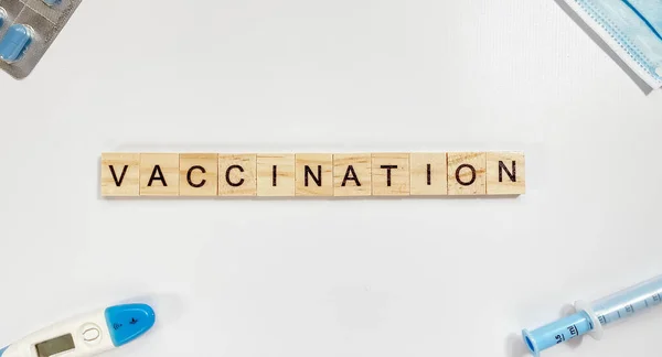 Rozvržení se slovem očkování z dřevěných písmen a v blízkosti injekční stříkačky, teploměru, lékařské masky a pilulek — Stock fotografie