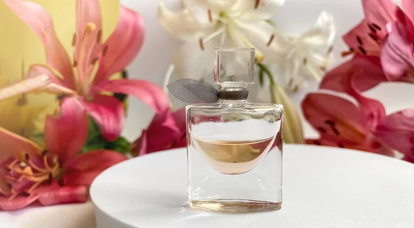 Parfum mit Blüten auf weißem Hintergrund. Eine Parfümflasche umgeben von Lilienblüten in rosa und weißer Farbe — Stockfoto