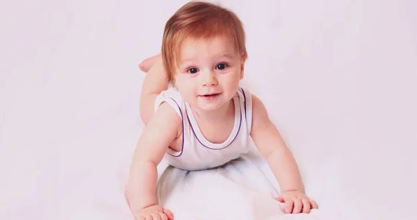 Um menino caucasiano jaz em um bodysuit branco com um brinquedo em um fundo branco — Fotografia de Stock