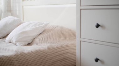 Odanın içi bej renginde yatak, yastık, dolap ve çiçeklerle dolu.