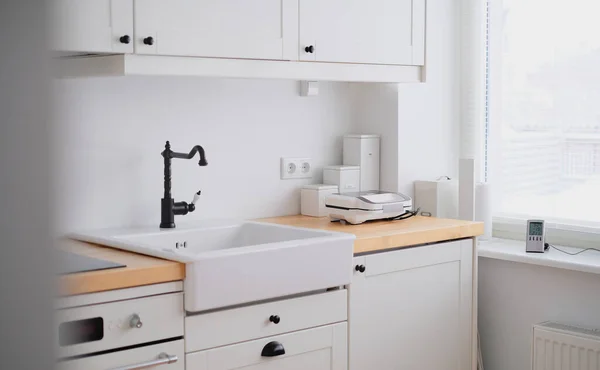 El interior de una cocina en tonos blancos con un fregadero, sándwich, estufa, horno, mesa de comedor y una ventana de luz —  Fotos de Stock