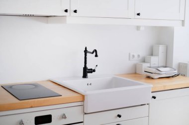 Lavabosu, sandviç makinesi, ocağı, yemek masası ve penceresi olan beyaz tonda bir mutfağın içi.