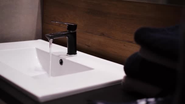 Close-up, badkamerinterieur, wastafel met spiegel, zwarte kraan en donkere handdoeken — Stockvideo