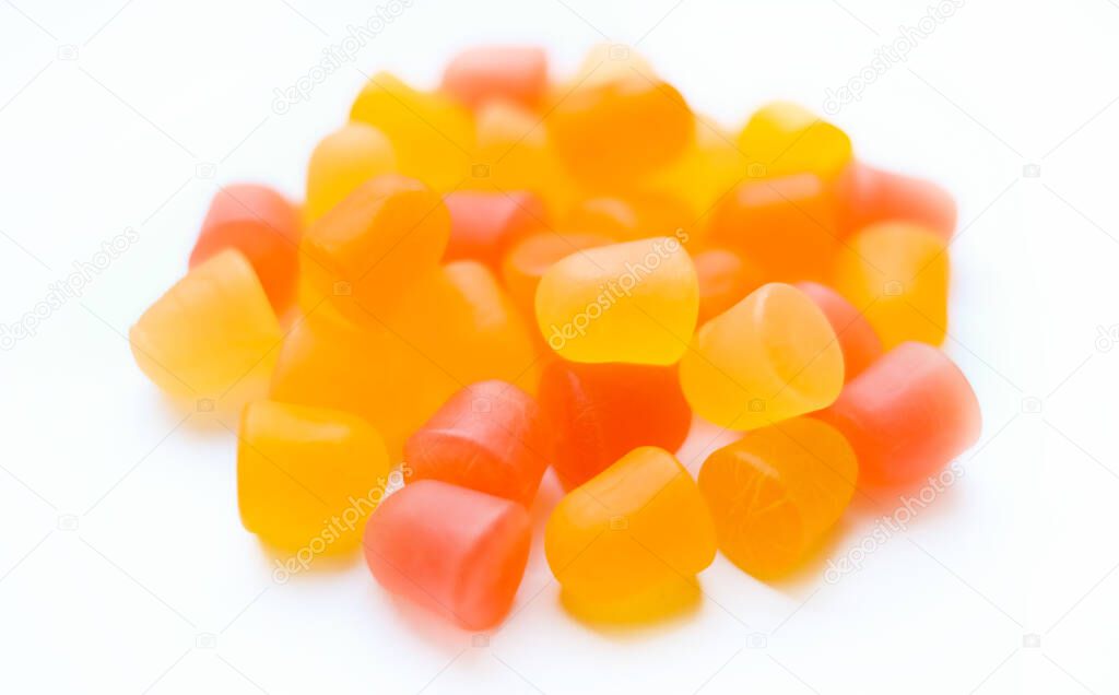 Close-up texture of orange and yellow multivitamin gummies in the form of bears on white background. 