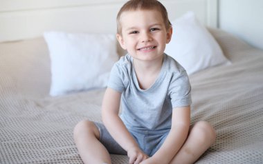 Gri tişörtlü, küçük, mutlu, beyaz bir çocuğu yakından çek ve yatağa uzan ve gülümse..