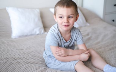 Gri tişörtlü, küçük, mutlu, beyaz bir çocuğu yakından çek ve yatağa uzan ve gülümse..