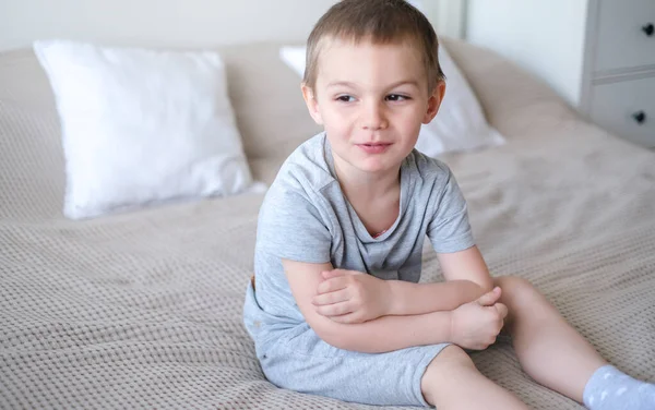 Gri tişörtlü, küçük, mutlu, beyaz bir çocuğu yakından çek ve yatağa uzan ve gülümse..