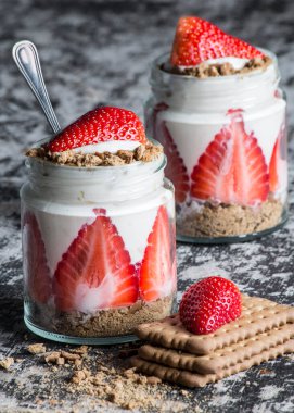Tahta bir tahtanın üzerinde yoğurt, çilek ve bisküvi bulunan iki cam kavanoz. Tatlı lezzetli.