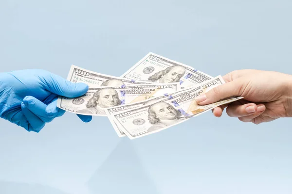 Man's hand giving money (dollars) to a hand in blue surgical glove, nurse or doctor. Corruption in medicine field.