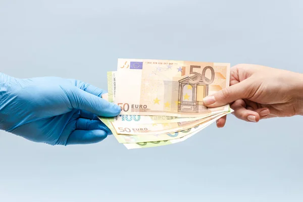 Man\'s hand giving money (euro) to a hand in blue surgical glove, nurse or doctor. Corruption in medicine.