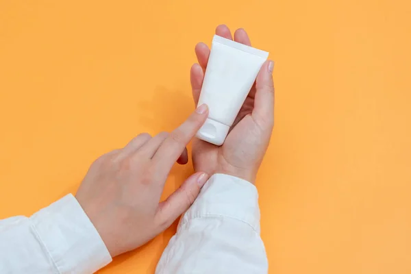 Cosmetic tube in hand in white coat with orange background. Cosmetics, beauty, medicine and spa concept