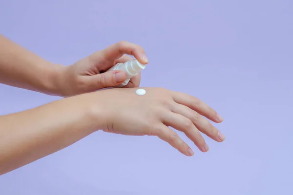 Woman's hand squeezing out cream in white tube isolated on lilac background. Beauty concept. Tube for cosmetic products