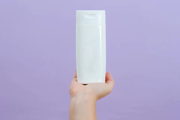 Cosmetic packaging tube in womans hand on lilac background. Beauty concept. Tube for cosmetic products