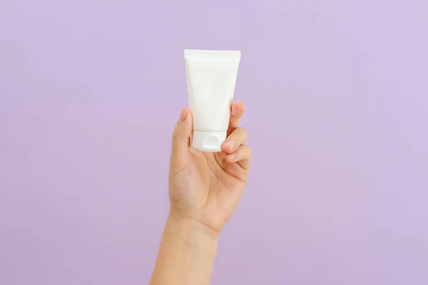 Cosmetic cream tube in womans hand on lilac background. Beauty concept. Packaging tube for cosmetic products