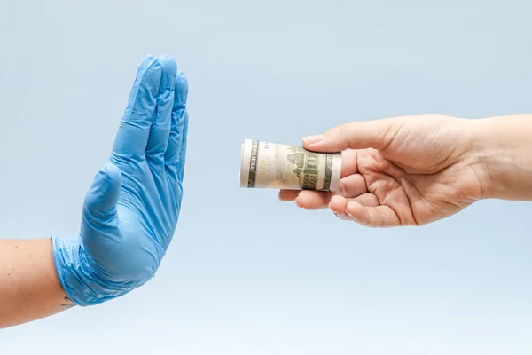 Offering money (dollars) to a hand in blue surgical glove, nurse or doctor. Corruption.