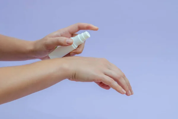 Woman\'s hand squeezing out cream in white tube isolated on lilac background. Beauty concept. Tube for cosmetic products