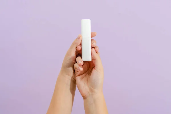 Cosmetic cream battle in womans hand on light lilac background. Beauty concept. Packaging tube for cosmetic products