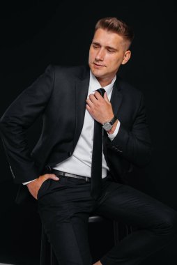 Siyah takım elbiseli ve siyah arka planda gülümseyen yakışıklı bir genç. Temizlen, hazırlan..