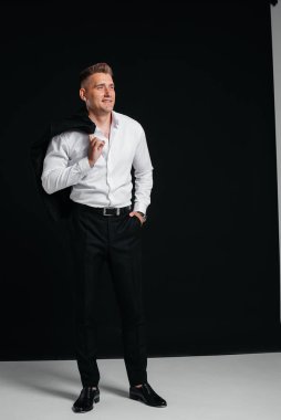 Yakışıklı genç bir adam ceketini çıkarıp siyah arka planda poz vererek gülüyor. Şık bir iş adamı. Büyük bir iş adamı..