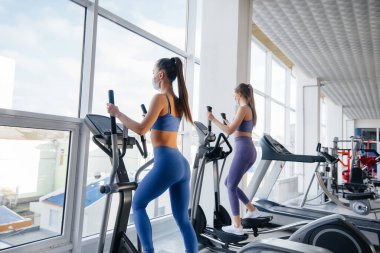 Salgın sırasında maske takan iki güzel kız spor salonunda egzersiz yapıyor. Halka açık yerlerde sosyal mesafeler.