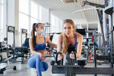 Salgın sırasında maske takan iki güzel kız spor salonunda egzersiz yapıyor. Halka açık yerlerde sosyal mesafeler.