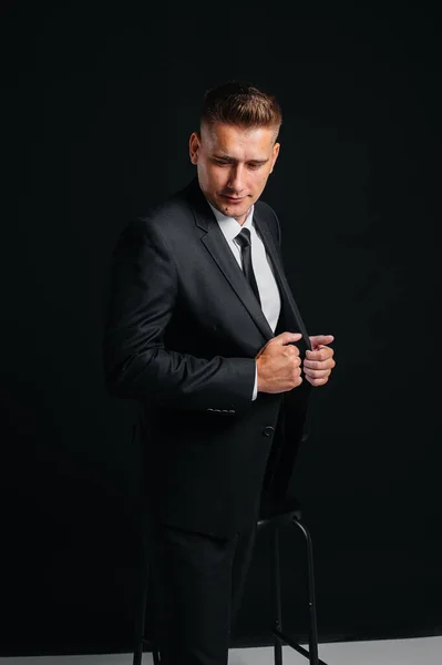 一个英俊的年轻人穿着时髦的黑色西服 在黑色的背景上微笑 — 图库照片