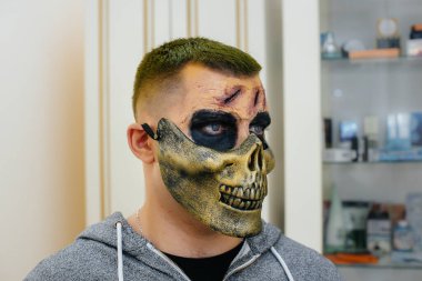 Cadılar Bayramı tatili için stüdyoda, kafatası şeklinde güzel, ürkütücü makyajlı genç bir adam. Mutlu Cadılar Bayramı konsepti.