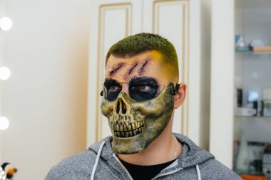 Cadılar Bayramı tatili için stüdyoda, kafatası şeklinde güzel, ürkütücü makyajlı genç bir adam. Mutlu Cadılar Bayramı konsepti.