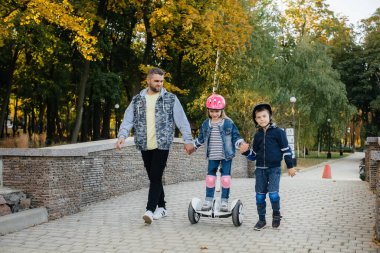 Bir baba gün batımında küçük çocuklarına Segway 'e binmeyi öğretir. Park 'ta aile tatili.