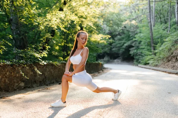 一个年轻漂亮的姑娘在日落时分 在茂密的森林里的路上 在训练前做了隆起和热身运动 健康的生活方式 呼吸新鲜空气 — 图库照片