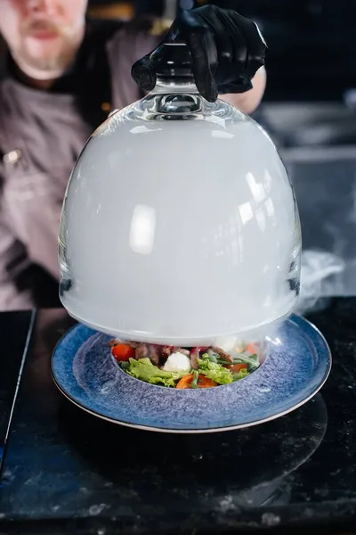 一位专业厨师在浓烟的玻璃罩下 提供新鲜的西红柿和小牛肉蔬菜沙拉 餐厅里烟熏得很美 — 图库照片