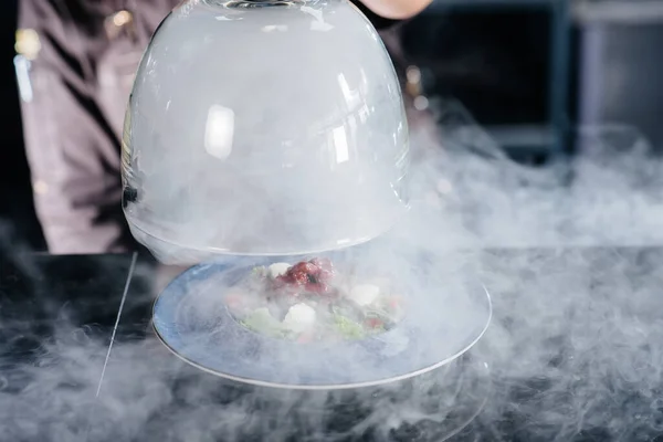 一位专业厨师在浓烟的玻璃罩下 提供新鲜的西红柿和小牛肉蔬菜沙拉 餐厅里烟熏得很美 — 图库照片